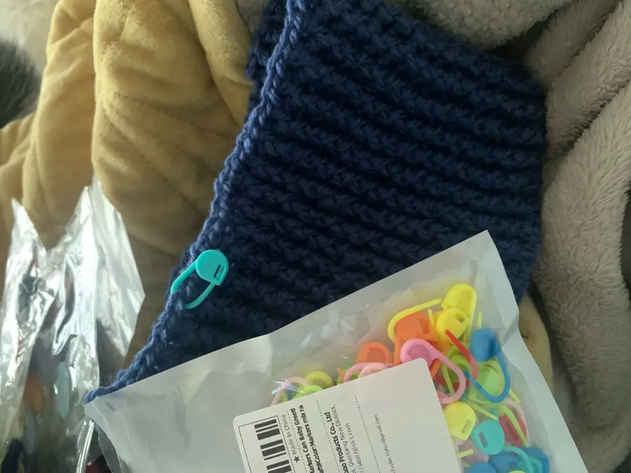 Buyer photo of a locking stitch marker clipped to the edge of navy knitting